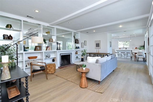 living room with light wood finished floors, visible vents, a fireplace with raised hearth, beamed ceiling, and recessed lighting