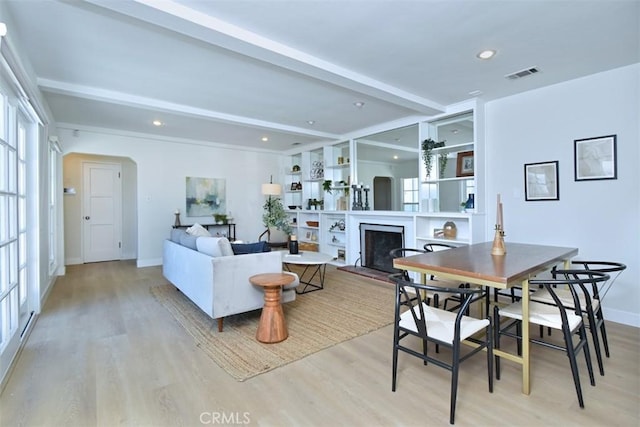 living room with plenty of natural light, visible vents, a fireplace with raised hearth, and beamed ceiling