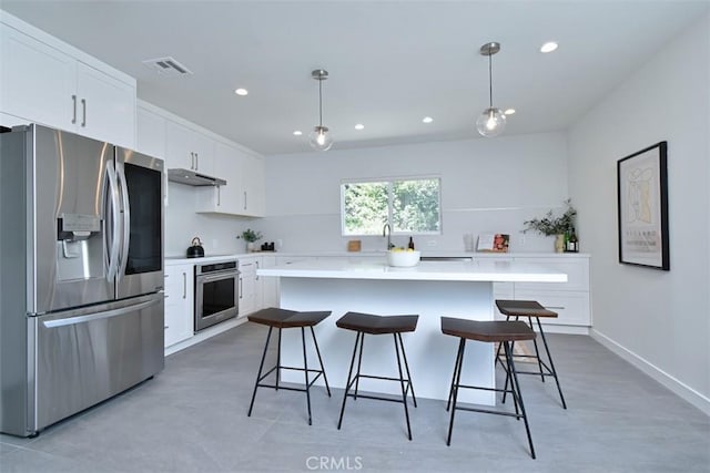 kitchen with stainless steel appliances, white cabinetry, under cabinet range hood, and a kitchen bar