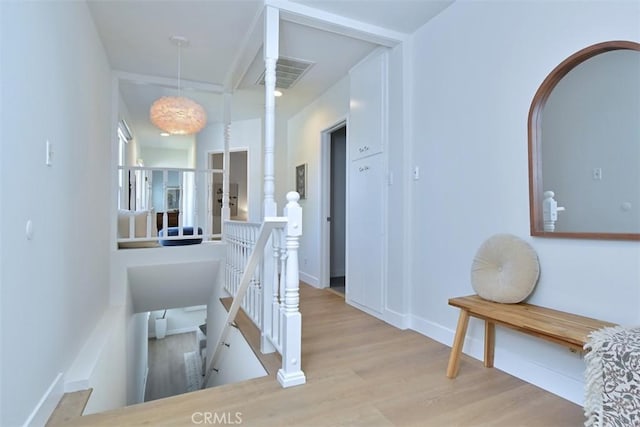 hallway with visible vents, wood finished floors, an upstairs landing, and baseboards