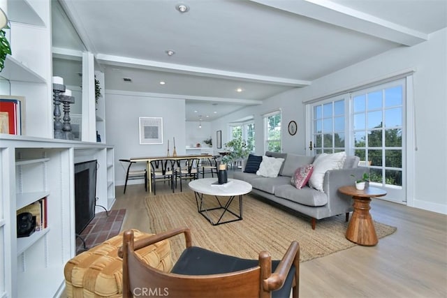 living area with a fireplace with flush hearth, beam ceiling, and wood finished floors