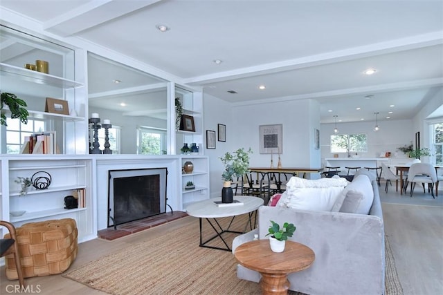 living area with a fireplace with raised hearth, recessed lighting, wood finished floors, built in features, and beamed ceiling