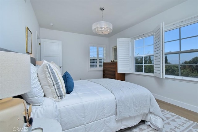 bedroom with lofted ceiling, an inviting chandelier, baseboards, and wood finished floors