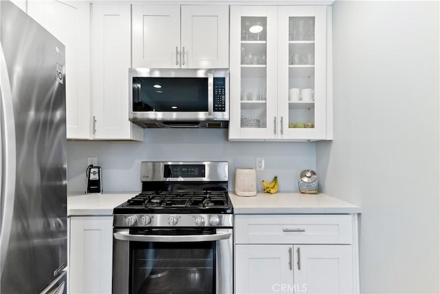 kitchen with appliances with stainless steel finishes, glass insert cabinets, and white cabinets