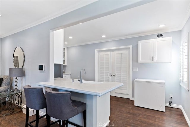 kitchen with dark wood-style flooring, a breakfast bar area, fridge, and white cabinetry