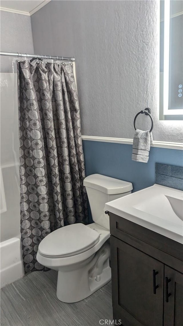 bathroom featuring a textured wall, toilet, shower / bathtub combination with curtain, crown molding, and vanity