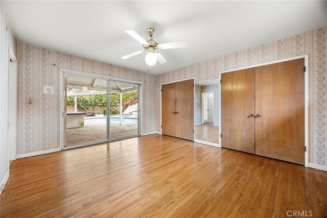 unfurnished bedroom with access to exterior, two closets, light wood-type flooring, baseboards, and wallpapered walls