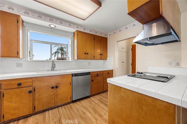 kitchen with cooktop, stainless steel dishwasher, light wood-type flooring, wall chimney range hood, and a sink