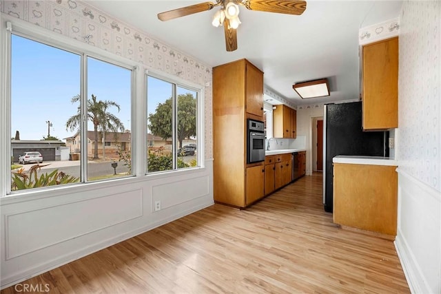 kitchen with light wood-style flooring, stainless steel appliances, light countertops, brown cabinets, and wallpapered walls