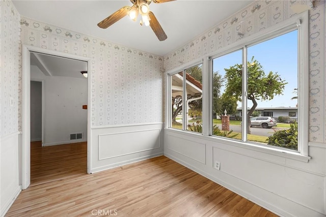 unfurnished room with light wood finished floors, visible vents, wainscoting, ceiling fan, and wallpapered walls