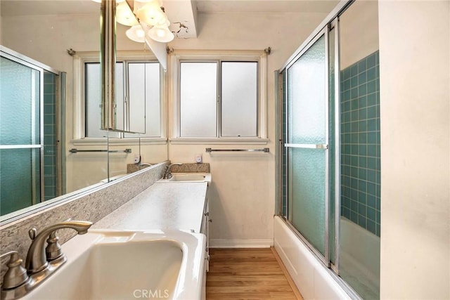 bathroom featuring enclosed tub / shower combo, a sink, baseboards, and wood finished floors