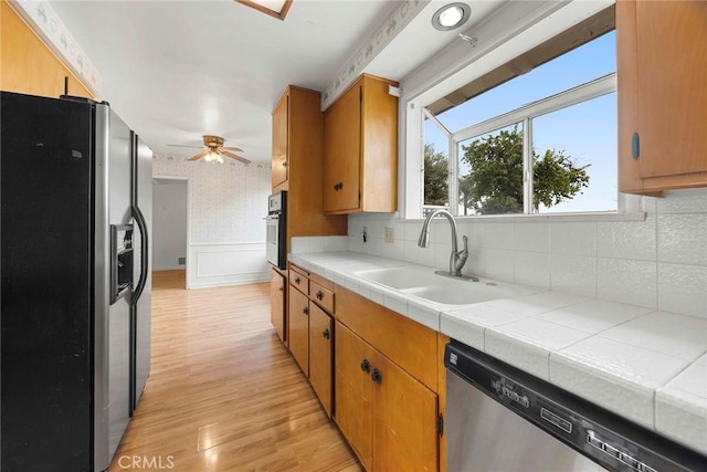 kitchen featuring a sink, light wood-style floors, appliances with stainless steel finishes, wainscoting, and wallpapered walls