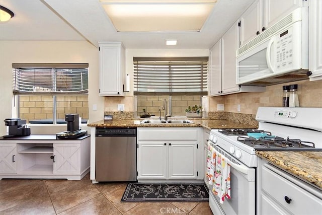 kitchen featuring white appliances, decorative backsplash, white cabinets, a sink, and a wealth of natural light