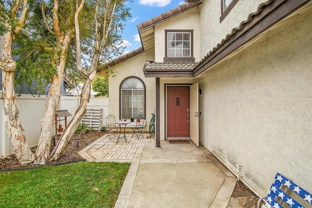 view of exterior entry with a patio area, fence, a tile roof, and stucco siding