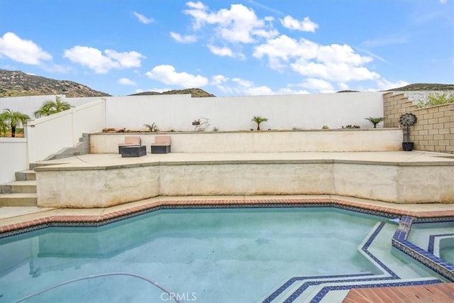 view of swimming pool with a fenced backyard, a pool with connected hot tub, and a mountain view