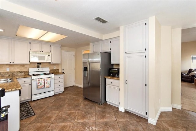 kitchen featuring stone counters, visible vents, a sink, white appliances, and baseboards