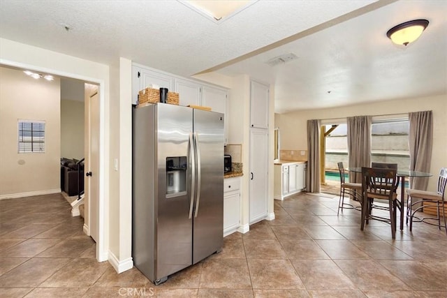 kitchen with light tile patterned floors, visible vents, white cabinets, and stainless steel fridge with ice dispenser