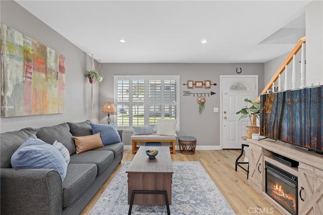 living area featuring baseboards, recessed lighting, a glass covered fireplace, and light wood-style floors