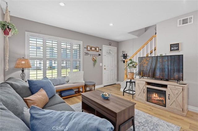 living room with baseboards, visible vents, stairs, light wood-type flooring, and recessed lighting