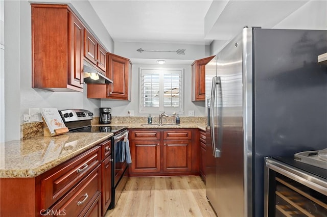 kitchen featuring light wood-style floors, appliances with stainless steel finishes, light stone countertops, under cabinet range hood, and a sink