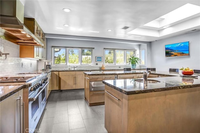 kitchen featuring wall chimney range hood, double oven range, a skylight, and dark stone countertops