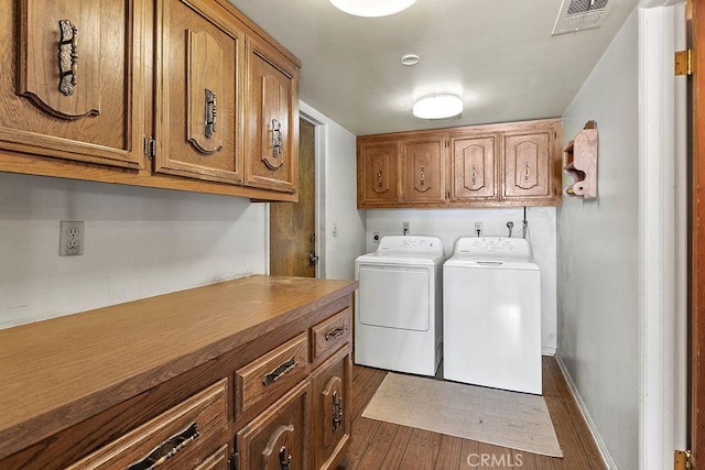 clothes washing area with cabinet space, visible vents, dark wood finished floors, baseboards, and washing machine and dryer