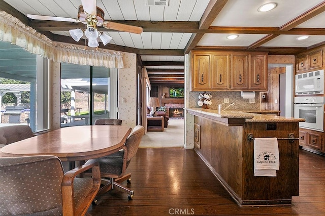 kitchen featuring a peninsula, white appliances, beam ceiling, brown cabinetry, and dark wood finished floors