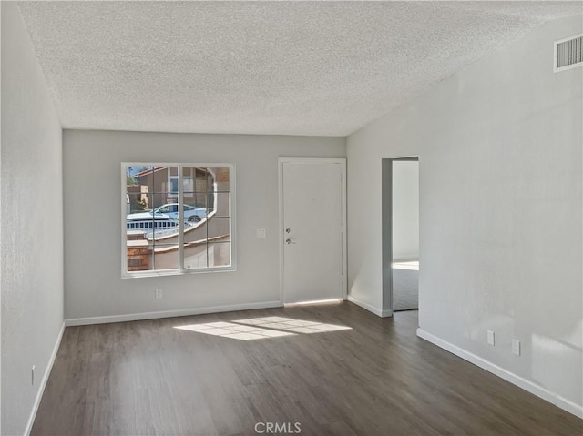 spare room featuring visible vents, a textured ceiling, baseboards, and wood finished floors