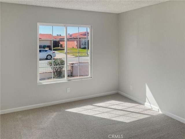 carpeted spare room featuring a textured ceiling and baseboards