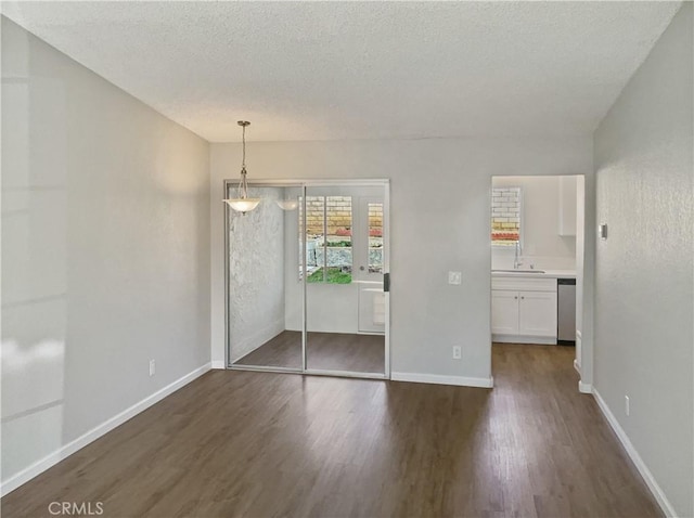 unfurnished dining area featuring a textured ceiling, baseboards, dark wood finished floors, and a sink