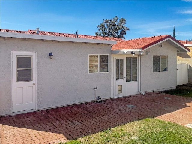 rear view of house with a patio area, a tile roof, and stucco siding