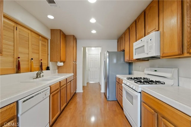 kitchen with white appliances, visible vents, a sink, light wood-style floors, and brown cabinets