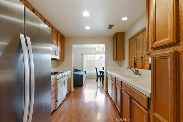 kitchen featuring white appliances, tile countertops, recessed lighting, a sink, and light wood-type flooring