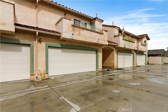 exterior space featuring stucco siding, a balcony, a garage, and a tile roof