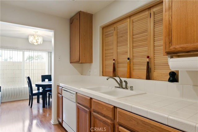 kitchen featuring brown cabinets, light wood-style flooring, a sink, white dishwasher, and tile counters