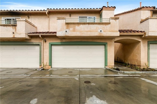 view of front of home with stucco siding, a balcony, a garage, and a tiled roof