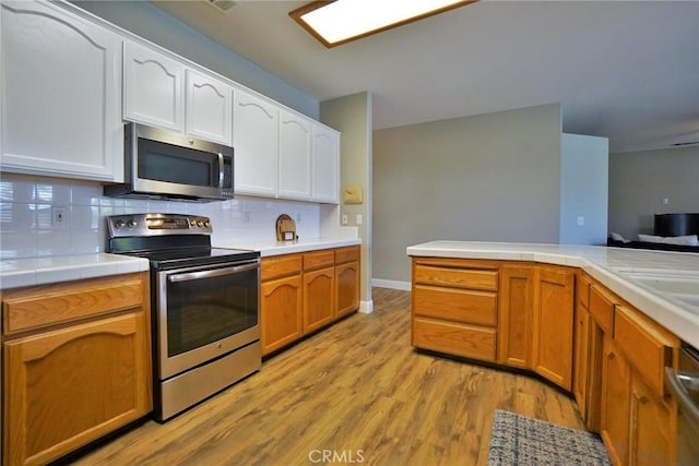 kitchen featuring white cabinets, tile countertops, light wood-style flooring, appliances with stainless steel finishes, and backsplash