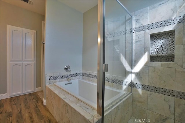 bathroom with a garden tub, visible vents, tiled shower, and wood finished floors