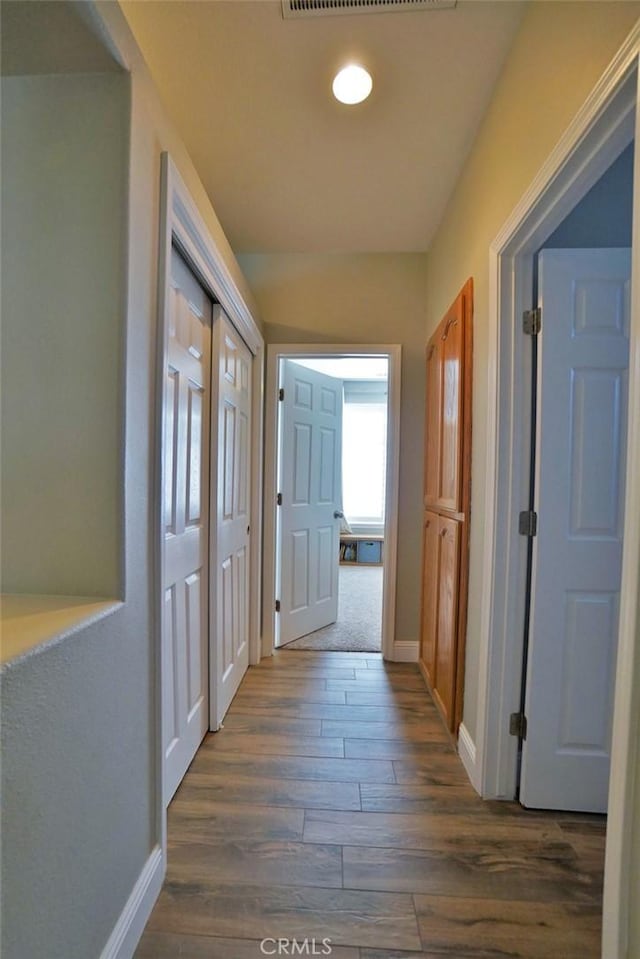 corridor featuring dark wood-type flooring and baseboards