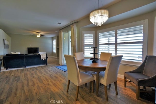 dining space with ceiling fan with notable chandelier, visible vents, baseboards, and wood finished floors