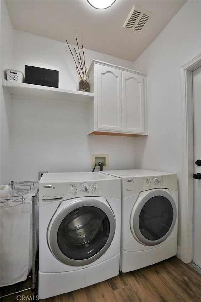 clothes washing area with cabinet space, visible vents, washer and dryer, and wood finished floors