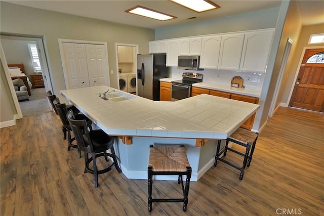 kitchen with appliances with stainless steel finishes, washer and dryer, a sink, and a kitchen breakfast bar