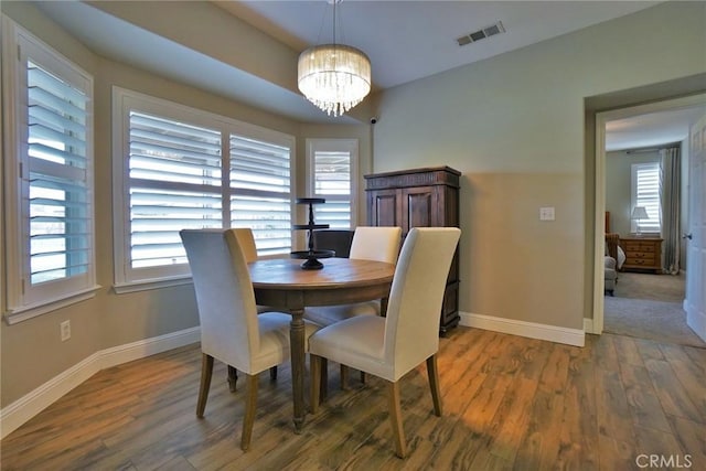 dining area with baseboards, wood finished floors, visible vents, and a notable chandelier