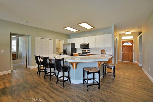 kitchen with tile countertops, stainless steel appliances, a breakfast bar, wood finished floors, and white cabinets