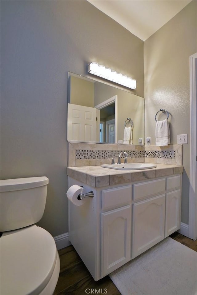 bathroom with baseboards, toilet, decorative backsplash, and wood finished floors