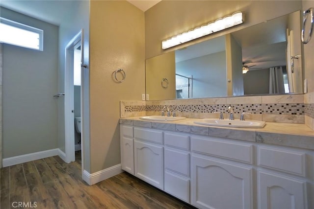 bathroom with tasteful backsplash, baseboards, a sink, and wood finished floors