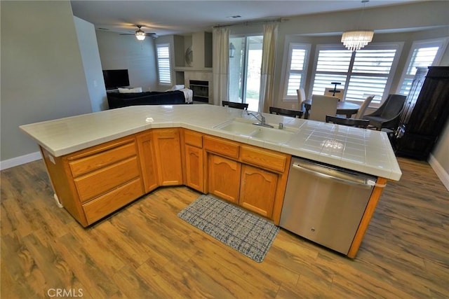 kitchen featuring tile countertops, wood finished floors, a sink, open floor plan, and stainless steel dishwasher