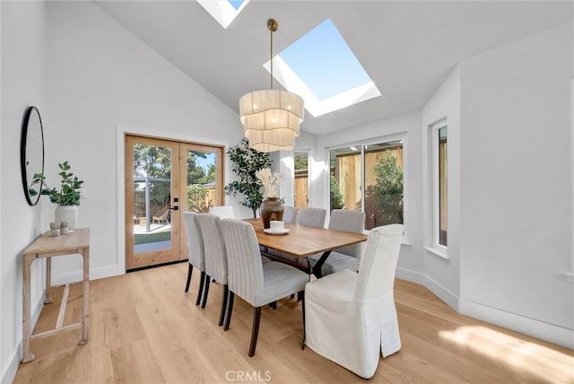 dining space featuring baseboards, light wood-type flooring, french doors, a skylight, and high vaulted ceiling