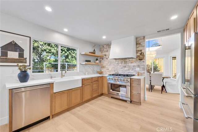 kitchen with visible vents, a sink, premium appliances, wall chimney exhaust hood, and light countertops