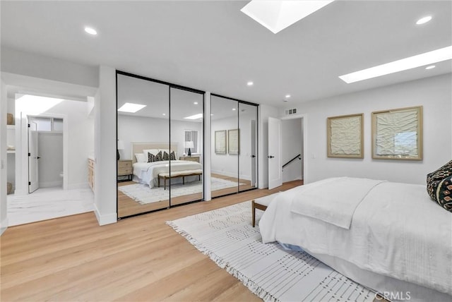 bedroom featuring a skylight, recessed lighting, multiple closets, and light wood finished floors